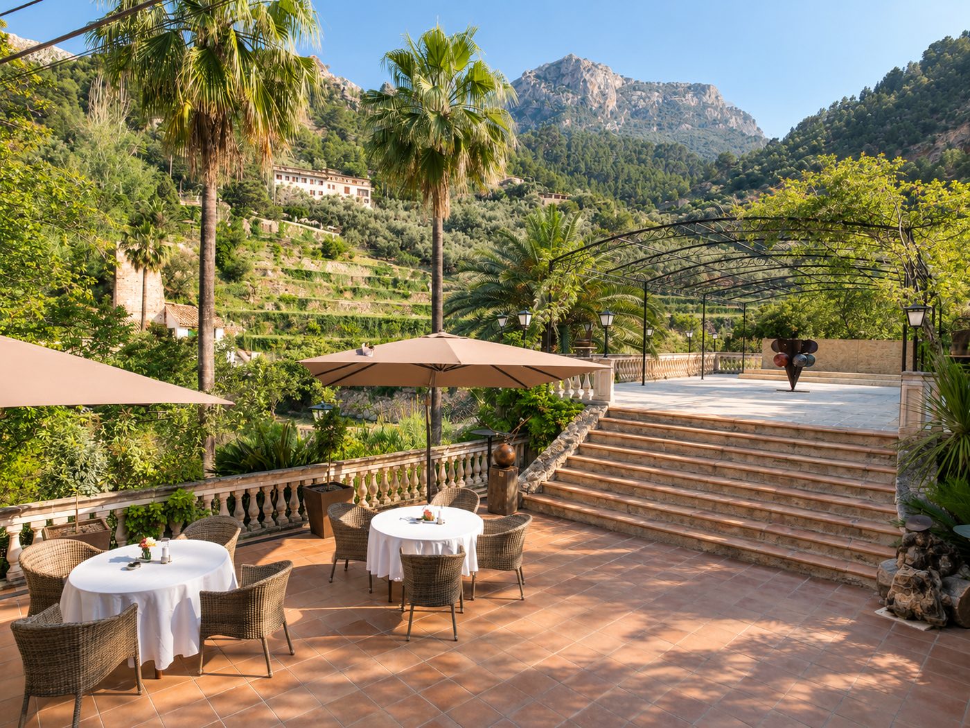 Terraza Deià con mesas bajo sombrillas, escalinata hacia La Pérgola y vistas a la Sierra de Tramuntana